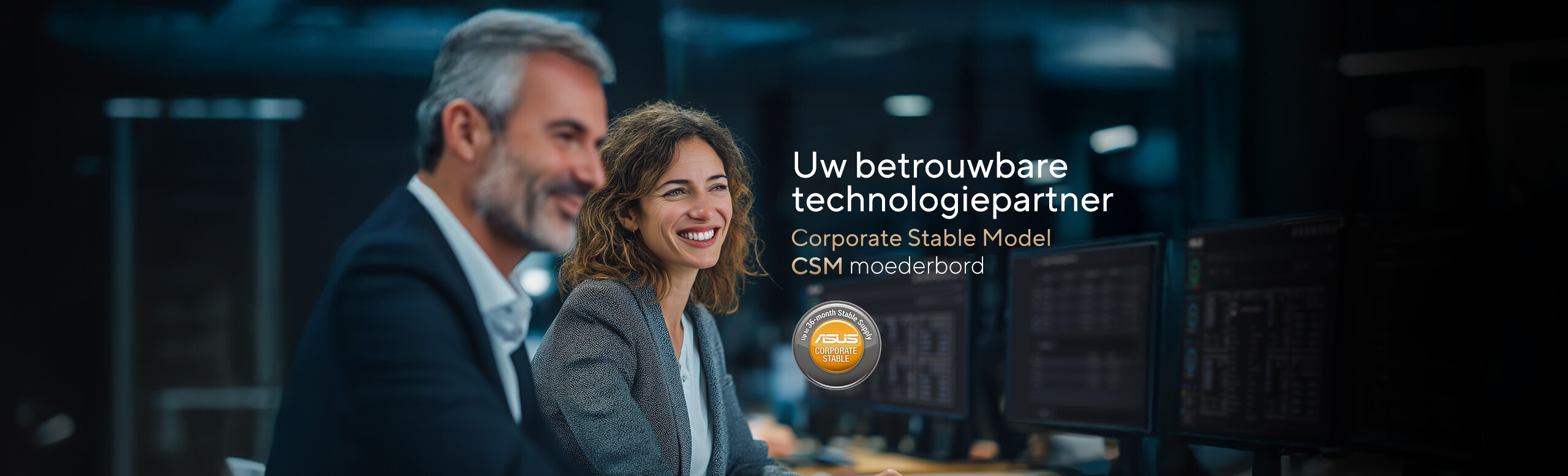 A man in a suit and a woman with wavy, light brown hair wearing a business jacket and white shirt are seated together at a desk in a modern office setting. Computer monitors are visible in the background, alongside promotional text for ASUS Corporate Stable Model (CSM) Motherboard: Your Trusted Technology Partner Program, and a circular badge stating 'Up to 36-month Stable Supply.'