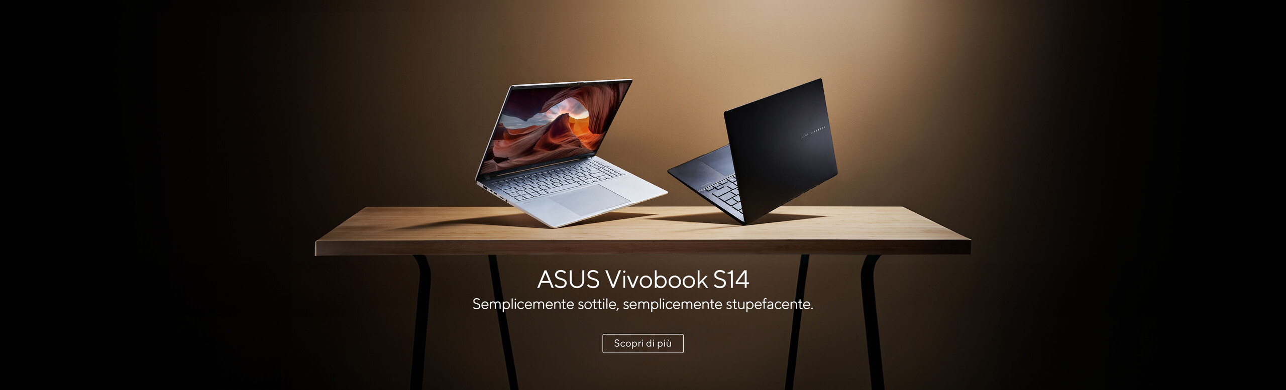 L'immagine mostra due laptop ASUS Vivobook S14 posizionati su un tavolo di legno. Uno dei laptop è aperto mostrando lo schermo, mentre l'altro è chiuso.