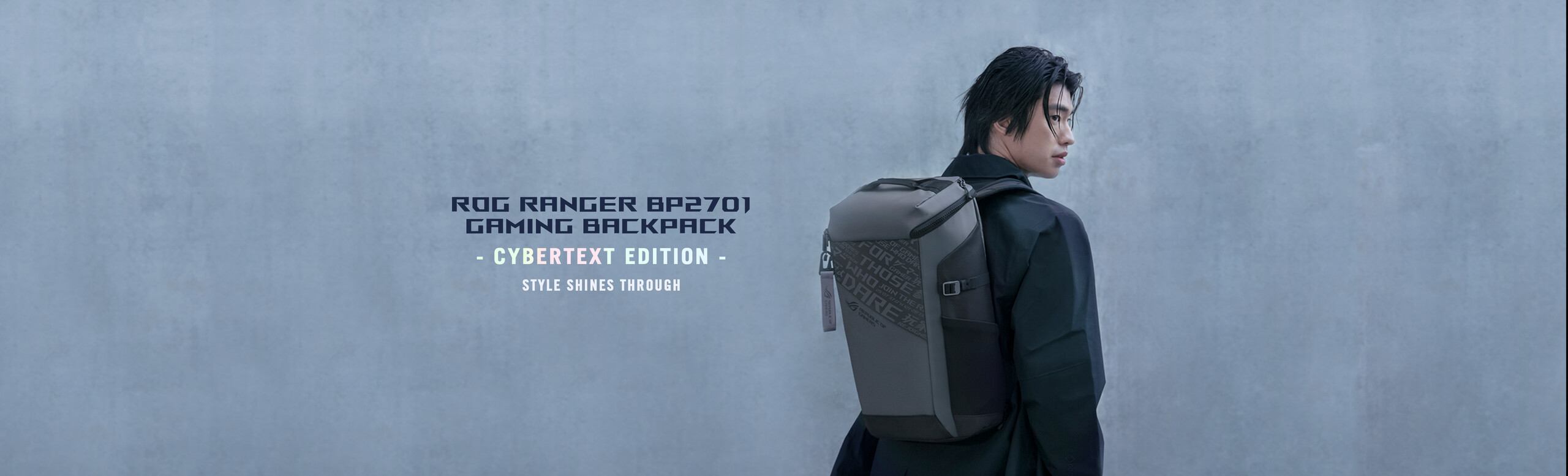 Una persona con una giacca scura in piedi vicino a un muro di cemento, che guarda alle sue spalle e indossa uno zaino da gaming ROG Ranger BP2701 con trama Cybertext